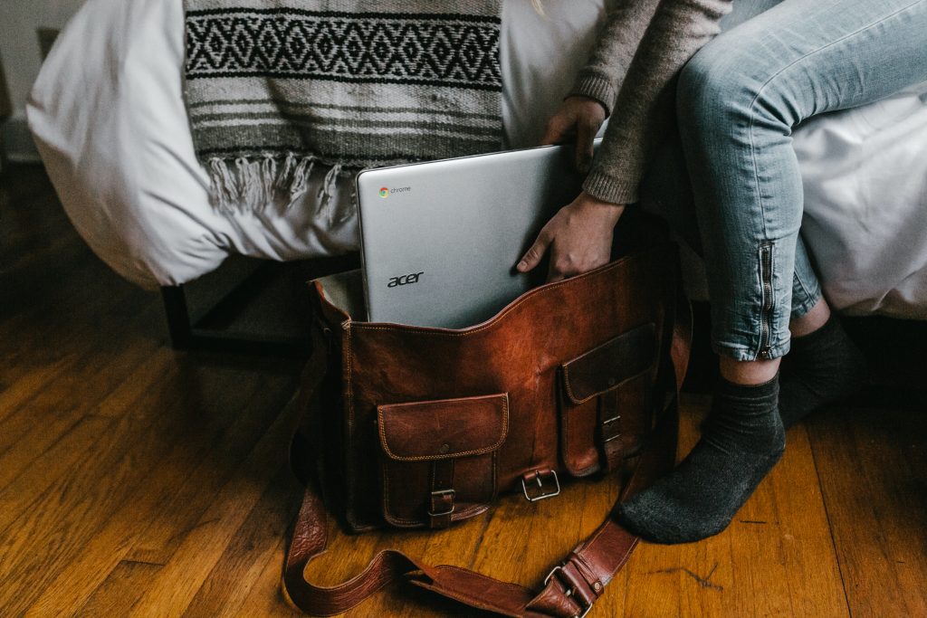 personne glisse laptop dans sac en cuir brun