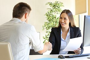 Jeune femme assise à un bureau qui donne la main à un homme pour conclure une entente