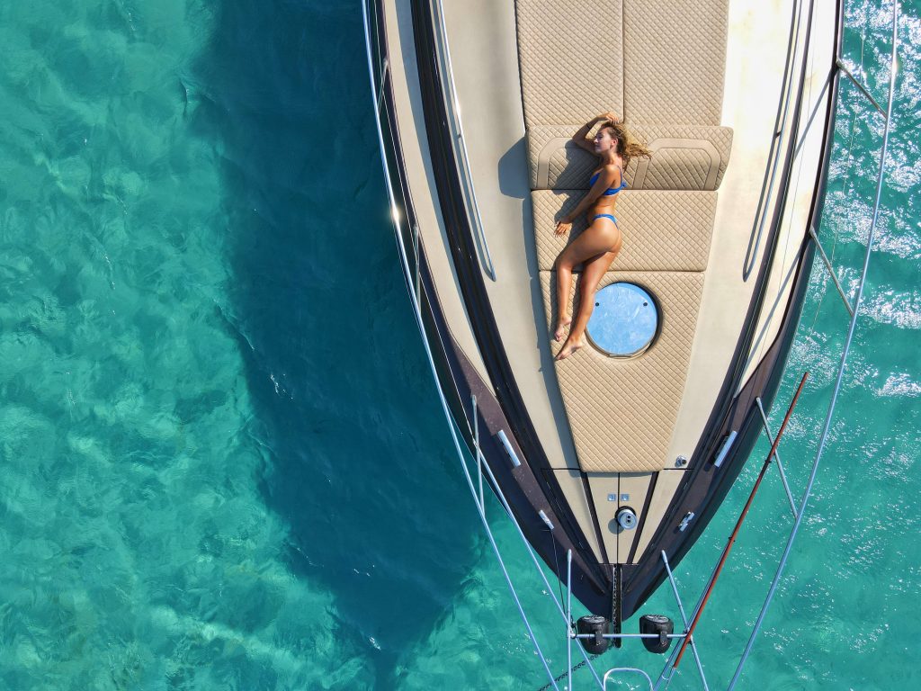 femme couchée en bikini sur le pont d'un yacht au milieu d'une eau turquoise