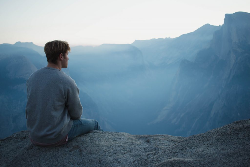 homme assis en contemplation devant paysage brumeux mais serein, médite en plein conscience